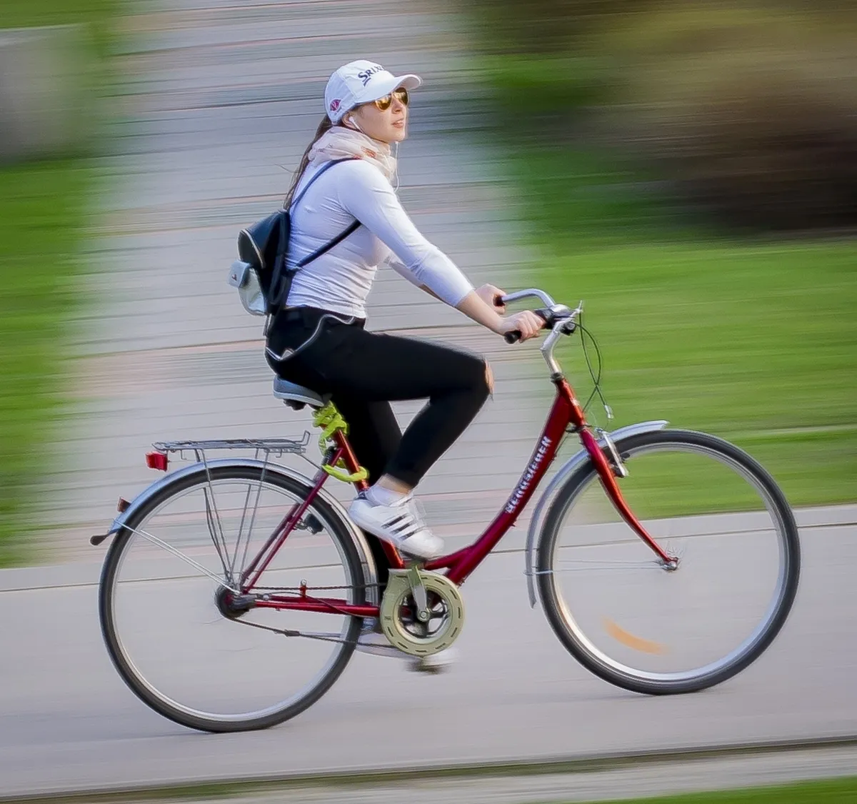 Woman in a white cap and sunglasses pedaling a red bicycle in soft motion blur